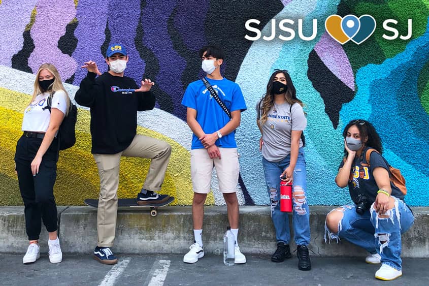 Students in SJSU gear posing in front of a colorful mural in downtown San Jose.